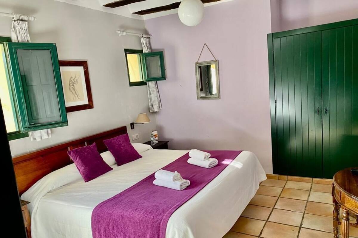 A bedroom with a bed, pillows, a bedside table, a lamp, and a green wardrobe.