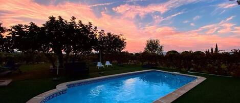 Una piscina con un diseño geométrico de mosaicos, rodeada de césped y árboles.
