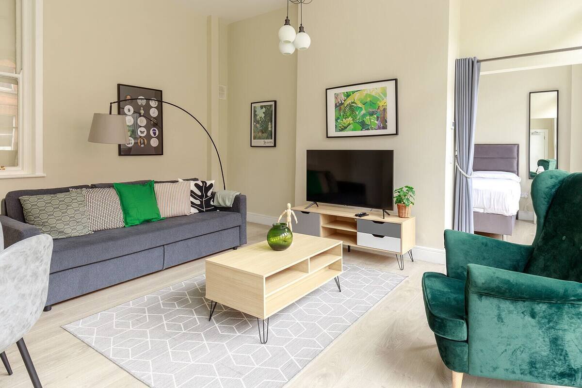 A modern living room with a grey sofa, a wooden coffee table, a green armchair, a TV, and artwork on the walls.