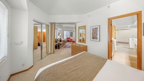 Una habitación de hotel con una cama grande, un aparador de madera, un sillón rojo, un sofá, un espejo y un baño con bañera y ducha.