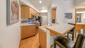 Cocina compacta con armarios de madera, microondas, refrigerador y un comedor con banco.