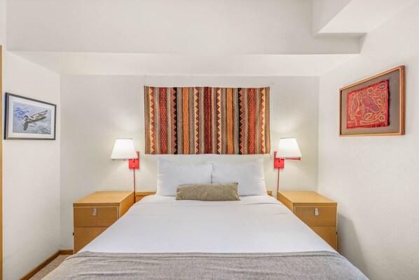 Habitación de hotel ordenada con una cama grande, dos mesitas de noche, cabecero con cortina estampada y dos lámparas fijadas a la pared.
