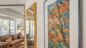 Una sala de estar con un cuadro grande enmarcados de hojas otoñales, un sofá, una mesa de centro y un espejo que refleja la habitación.