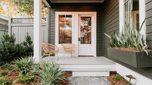 A porch with two wicker chairs, a white door, and a planter with plants. - The Springs Hotel (Ocean Springs)