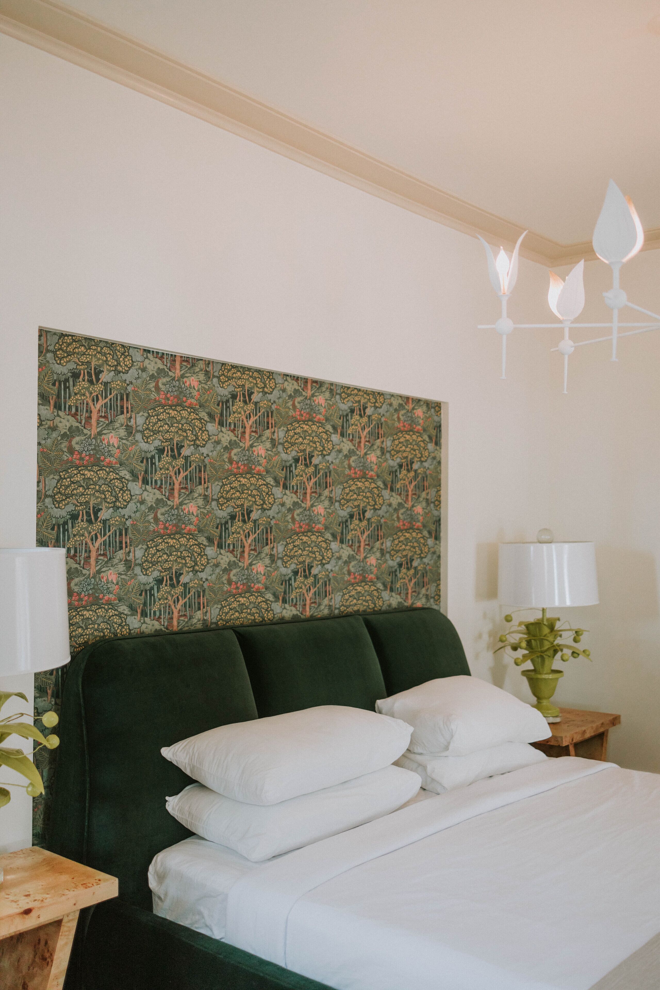 A neatly made bed with white linens and a green upholstered headboard.