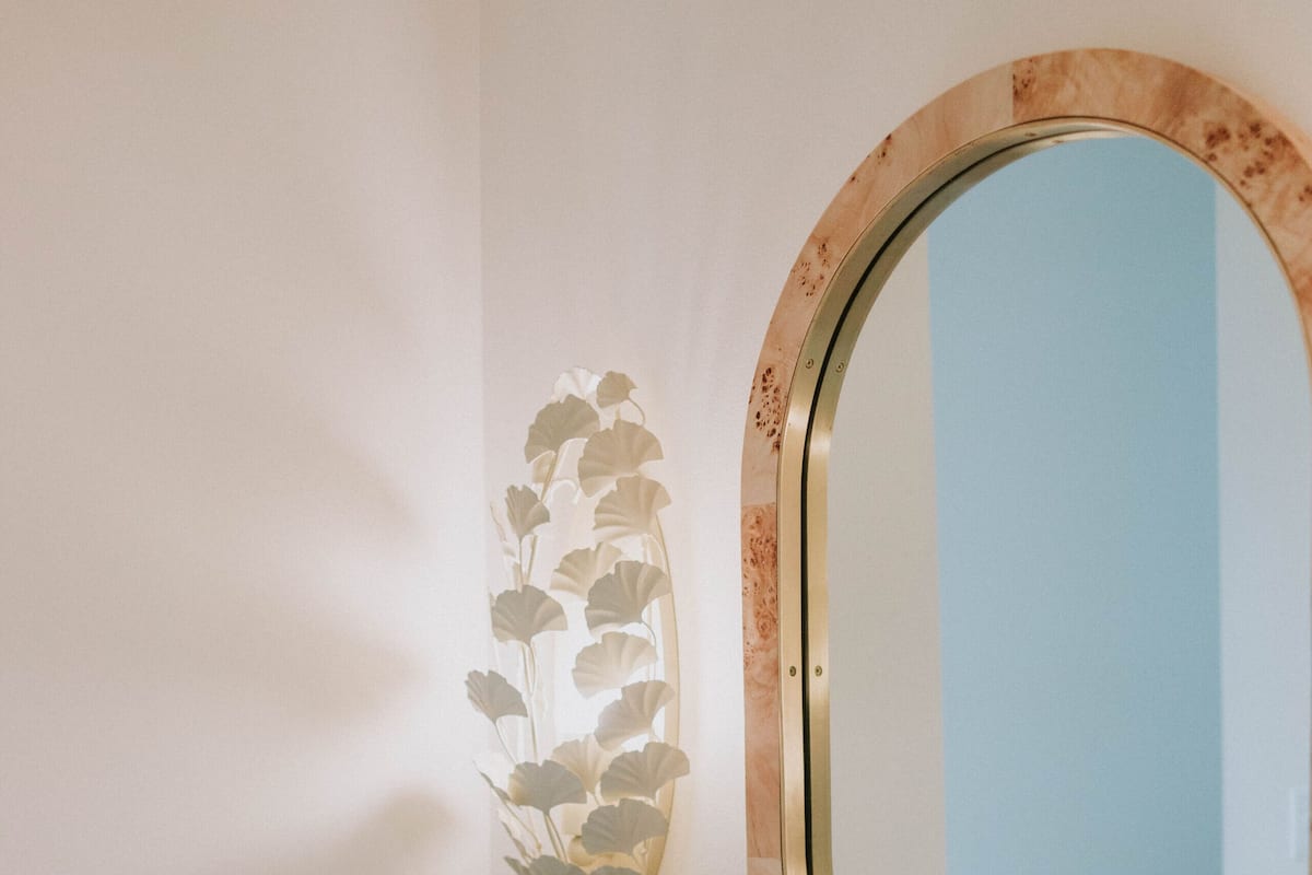 A bathroom with a marble sink, a mirror with a wooden frame, and a wall decoration of leaves.