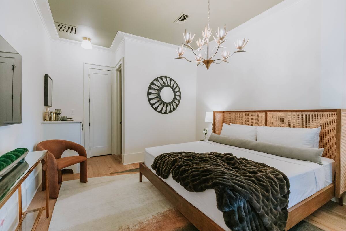 A bedroom with a large bed, a desk, a chair, a mirror, and a chandelier.