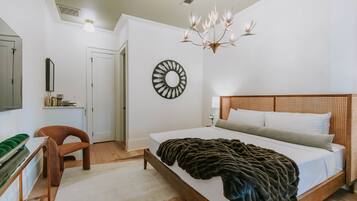 A bedroom with a large bed, a desk, a chair, a mirror, and a chandelier.