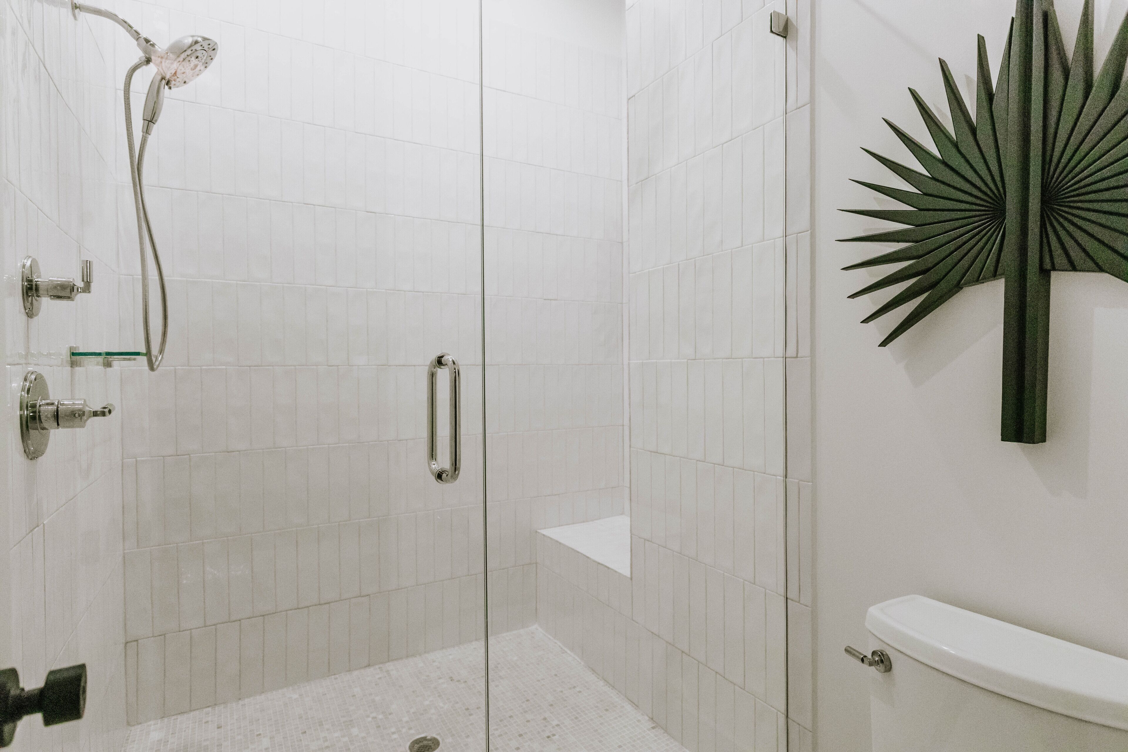 Ein modernes Badezimmer mit einer gläsernen Duschkabine, weißen Fliesenwänden und einem dekorativen Spiegel im Sonnenstrahl-Design.