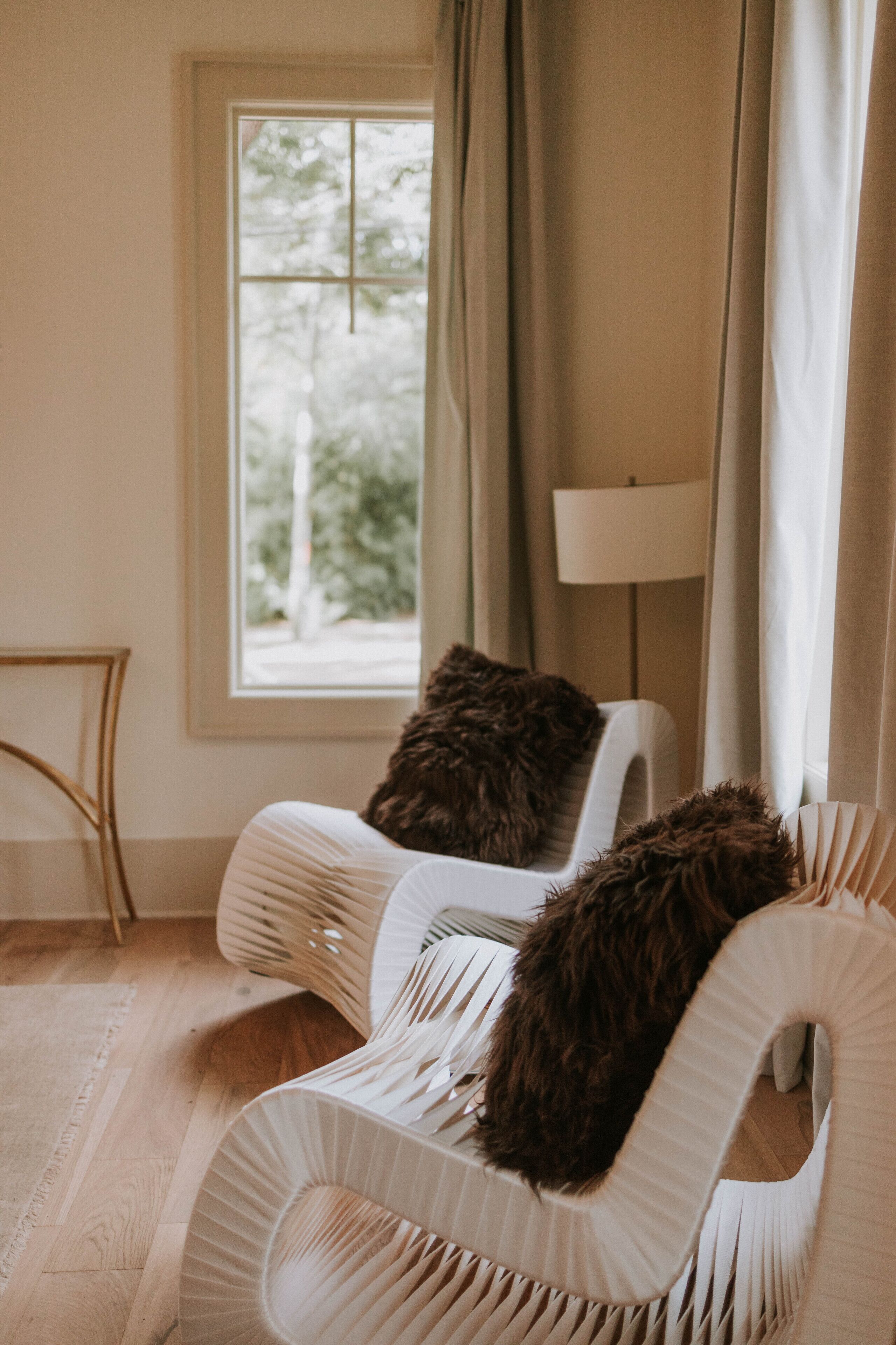A room with a window, a chair with a fluffy pillow, and a lamp.