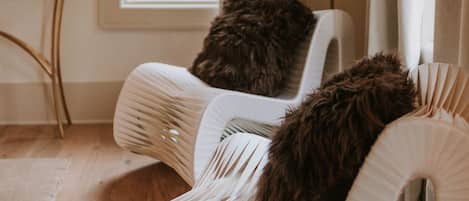 A room with a window, a chair with a fluffy pillow, and a lamp.