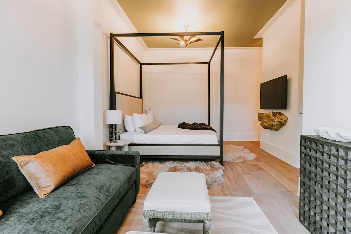 A modern bedroom with a four-poster bed, a green sofa, a white bedside table, and a mounted TV.