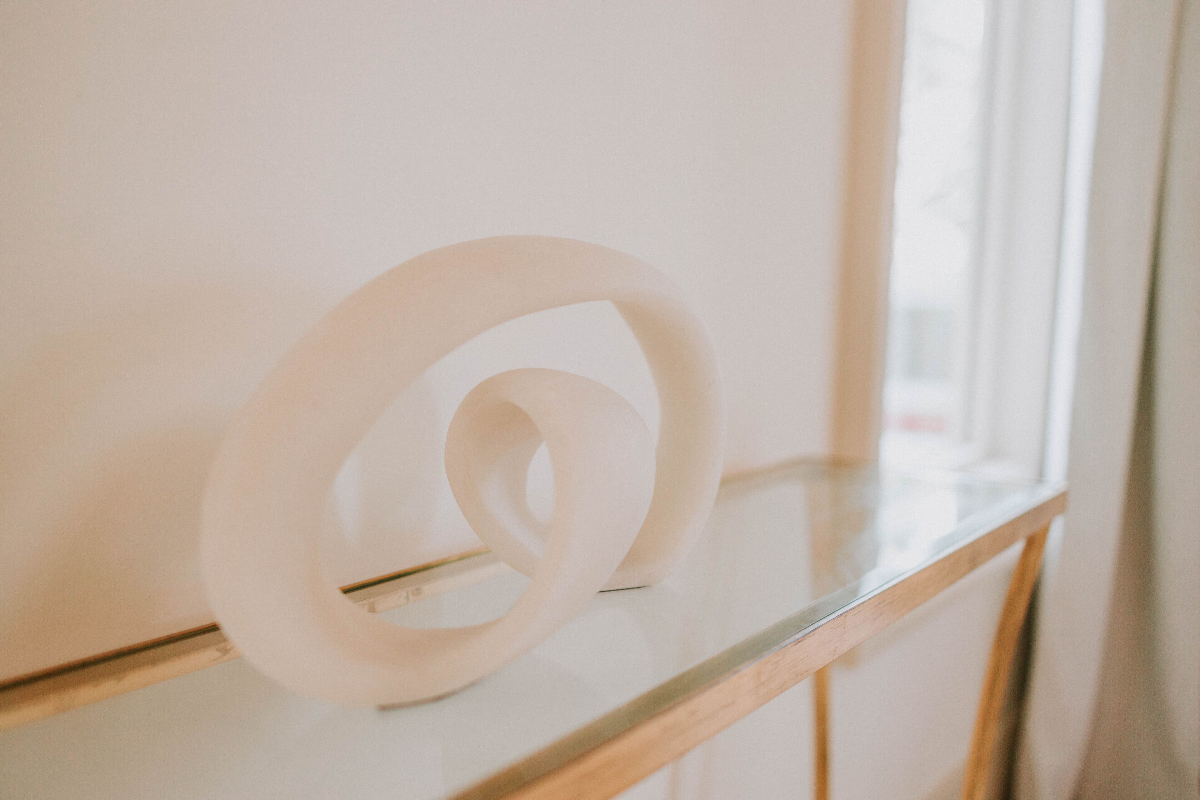 A white, abstract sculpture on a glass surface near a window.