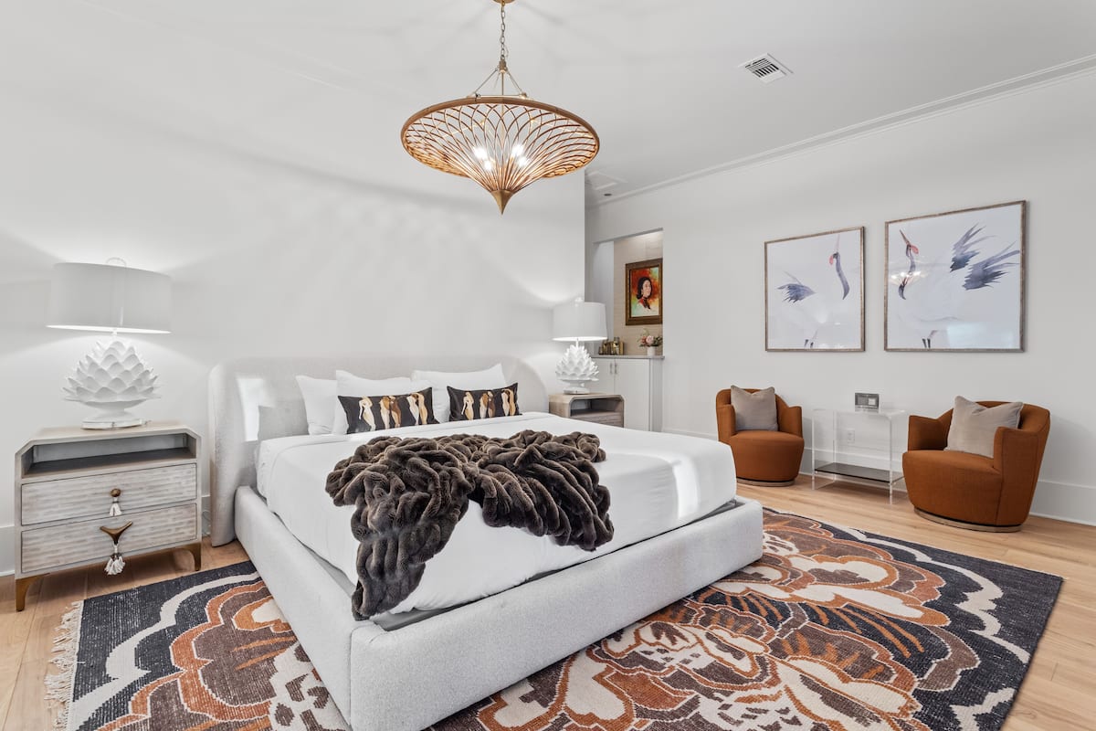 A modern bedroom with a large bed, a patterned rug, and two framed pictures on the wall.