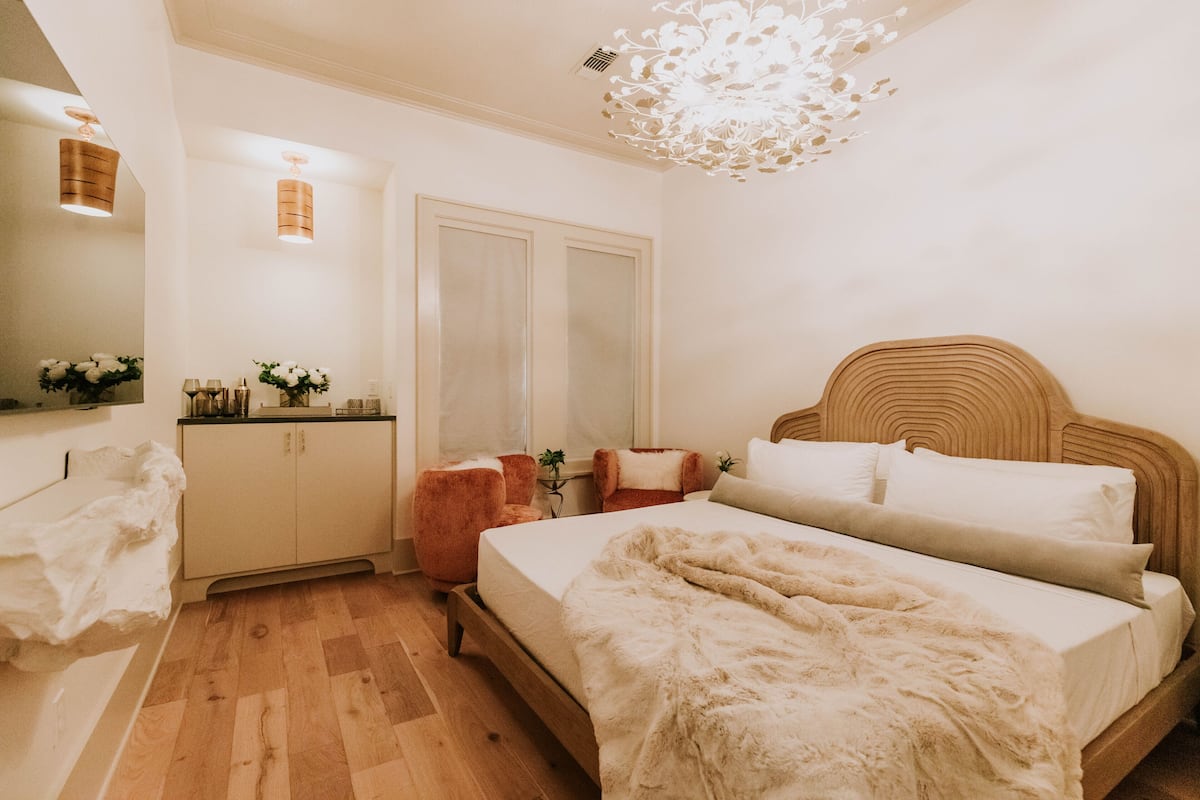 A bedroom with a wooden bed, a bedside table, a chair, a mirror, and a ceiling light fixture.