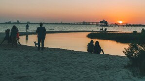 A beach scene with people walking and sitting near the water during sunset. - The Springs Hotel (Ocean Springs)