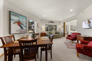 A living room with a dining area, a fireplace, and a large window. - Slopeview End | End-Unit King 1BD, Views, 159 (Olympic Valley)
