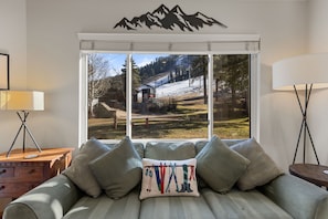 A room with a bed, a window with a mountain view, a lamp, and a wooden nightstand.