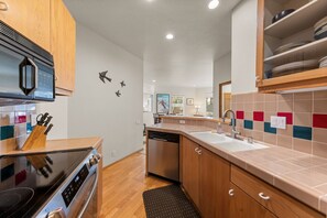 Eine moderne Küche mit Einbauofen, Mikrowelle und Geschirrspüler. Es gibt Holzschränke, eine geflieste Rückwand und einen schwarzen Teppich auf dem Boden.