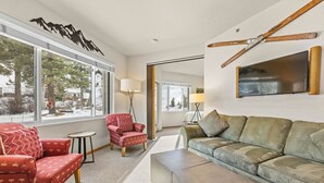 A living room with a large window, a red armchair, a green sofa, and a wooden ceiling fan.