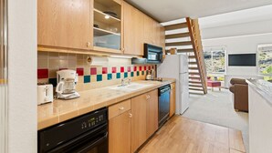 Een moderne keuken met houten kastjes, een vaatwasser, een koffiezetapparaat en een magnetron. Er is een raam met uitzicht op de omgeving.