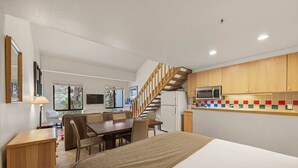 Un dormitorio moderno y compacto con una cama grande, un escritorio de madera y una zona de comedor.