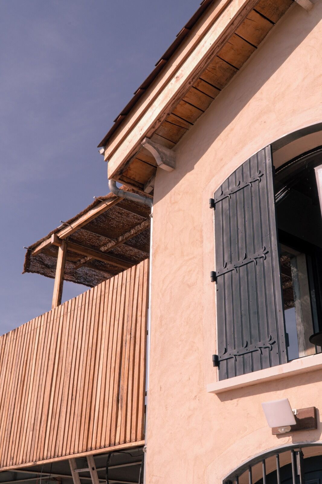 Een gebouw met een houten balkon en een raam met zwarte luiken.