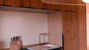 Une cuisine avec des meubles de rangement en bois, un plan de travail noir, un évier et un luminaire suspendu.