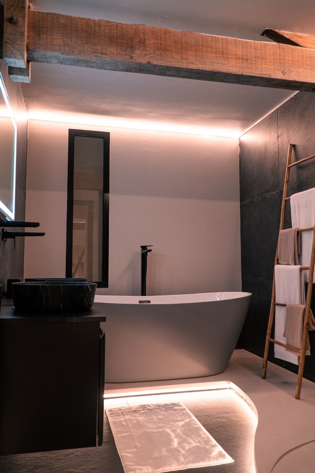 Een moderne badkamer met een vrijstaand bad, een grote spiegel en een handdoekhouder.