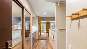 A hallway with wooden flooring, a wooden door, and a view of a living area with a couch and a plant. - 334 | Mtn Loft Escape w/ A/C - Fridge, Tubs & Gym (Olympic Valley)