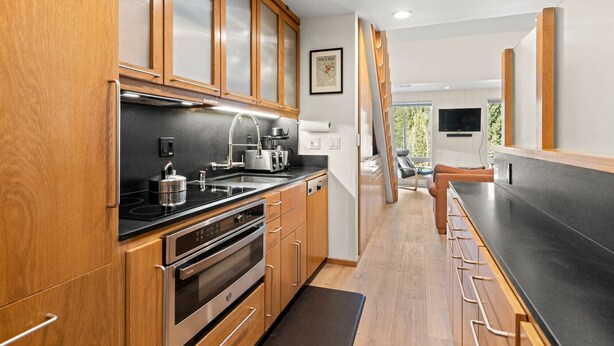 Une cuisine moderne avec des meubles en bois, un plan de travail noir, des appareils en acier inoxydable et un coin bar avec des tabourets.
