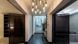 Un pasillo moderno con piso de madera oscura, una puerta de vidrio a la izquierda y un mueble negro a la derecha.