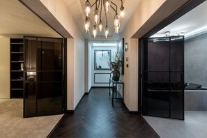 Un pasillo moderno con piso de madera oscura, una puerta de vidrio a la izquierda y un mueble negro a la derecha.