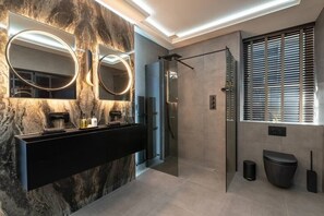 Un bany modern amb una paret de marbre, un lavabo negre i un espai de dutxa amb envà.