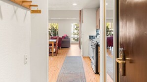 Un couloir étroit avec un plancher en bois, un tapis, un coin repas avec une table et des chaises, et un coin cuisine avec un réfrigérateur et une cuisinière.
