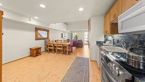 Une cuisine moderne avec des meubles en bois, une cuisinière en acier inoxydable et un coin repas comprenant une table et des chaises en bois.
