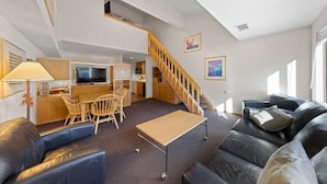 A modern living room with a sofa, a coffee table, a TV, and a staircase leading to an upper level. - 314 | Loft Escape - King Bed, Views, Hike & Bike (Olympic Valley)