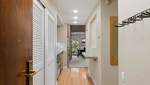 Un couloir doté d’un plancher en bois, de murs blancs et d’une porte avec des stores horizontaux.