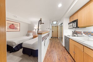 Una habitación de hotel compacta con dos camas, un kitchenette y un baño.