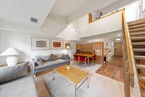 Un salon moderne avec un canapé, une table basse et des fauteuils rouges. Un escalier mène à un niveau supérieur.