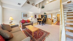 A spacious living area with a sofa, coffee table, and a dining table. A staircase leads to an upper level.