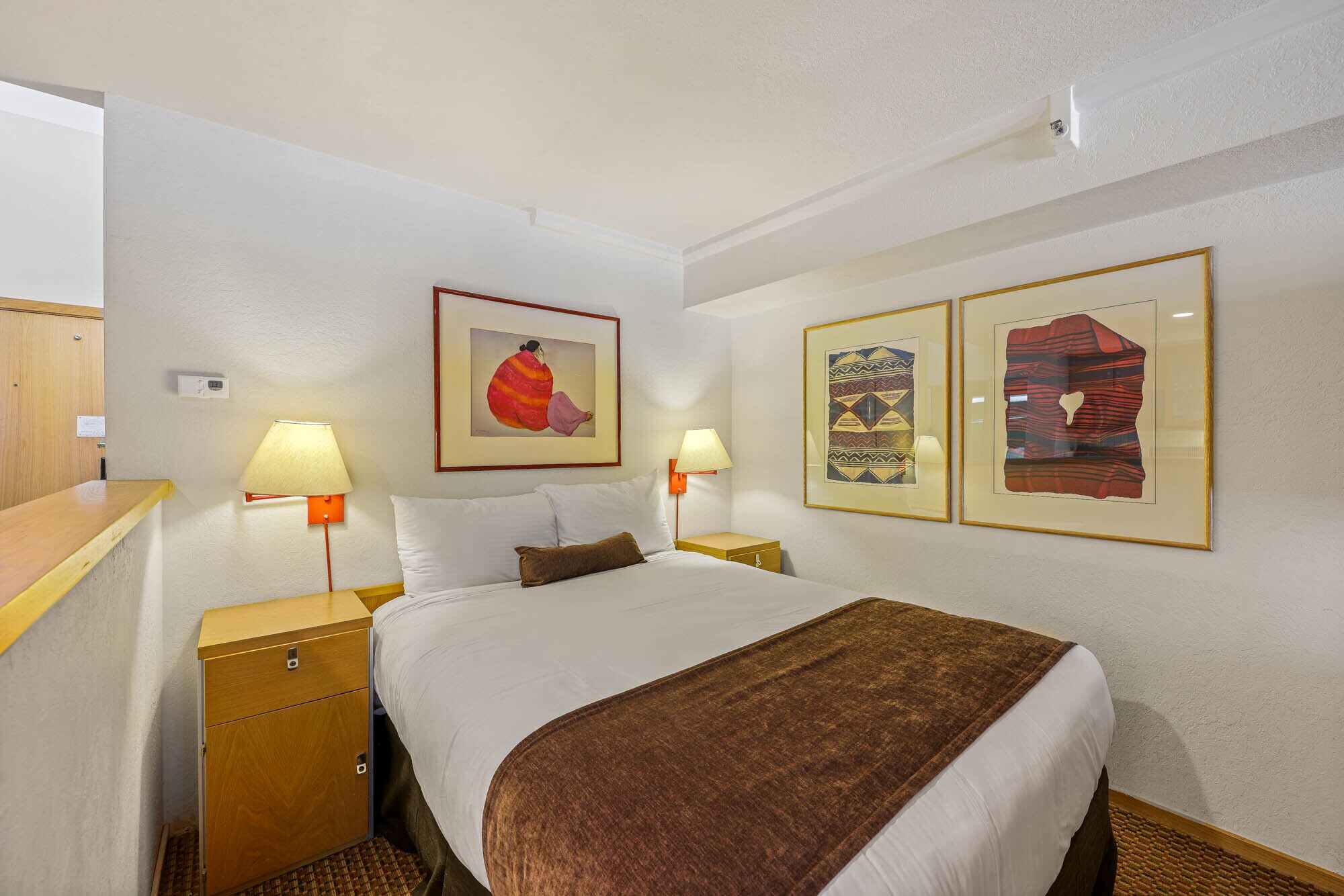 Ein Hotelzimmer mit einem Bett, zwei Nachttischen, einem Holznachtschränkchen und zwei Wandleuchten.