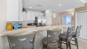 A modern kitchen with white cabinets, a stainless steel refrigerator, and a breakfast bar with four chairs.