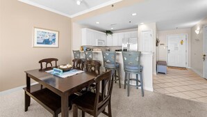 A dining area with a wooden table and chairs, a kitchen with white cabinets, and a tiled floor.