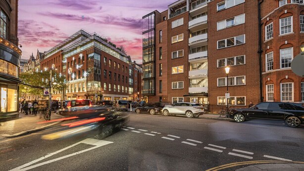 Une vue de rue présentant un mélange d’architecture moderne et traditionnelle, notamment un imposant bâtiment en briques rouges doté de nombreux balcons et une structure à façade de verre ornée de motifs en étoile.