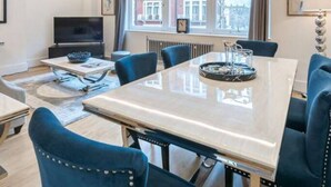 Un salon moderne doté d’une grande table à manger, de sièges confortables, d’un téléviseur à écran plat et offrant une vue sur la ville grâce à de grandes fenêtres.