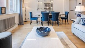 Un salon moderne avec un coin repas, comprenant un canapé blanc, des fauteuils bleus et une table centrale agrémentée d’un vase décoratif.