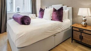 Une chambre d’hôtel moderne avec un grand lit, une table de chevet avec une lampe et une fenêtre avec des rideaux.