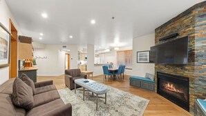 Ein modernes Wohnzimmer mit Kamin, Essbereich und einer Küche im Hintergrund.