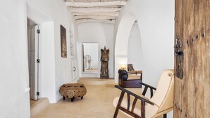 Un corridoio con una porta in legno rustica, uno sgabello di vimini, una poltrona a dondolo e una statua.